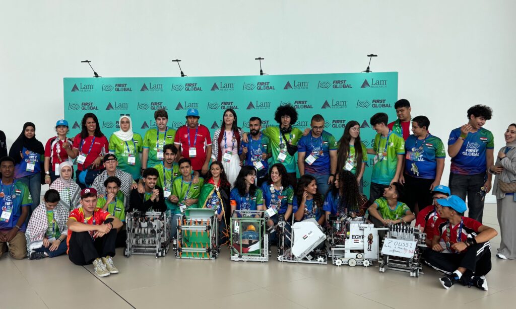 A Group Of Students And Adults From Different Countries Pose With Robots In Front Of Signage For The First Global Robotics Compe 1 Scaled