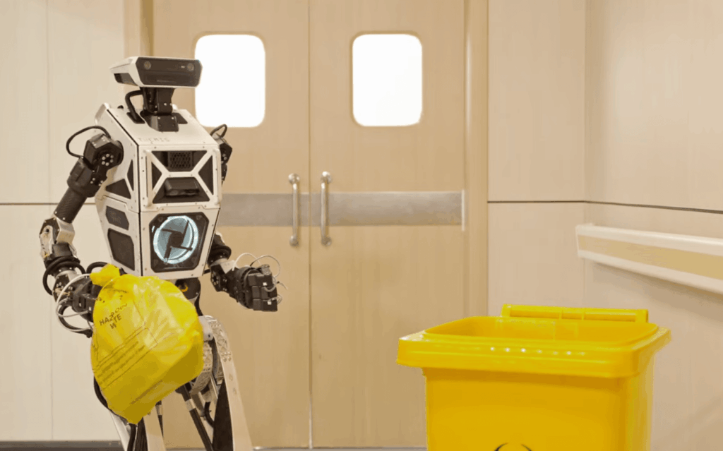 humanoid-robot-holds-small-yellow-bag-near-biohazard-trash-bin-in-a-hallway – Robótica, Inteligencia Artificial, Automatización